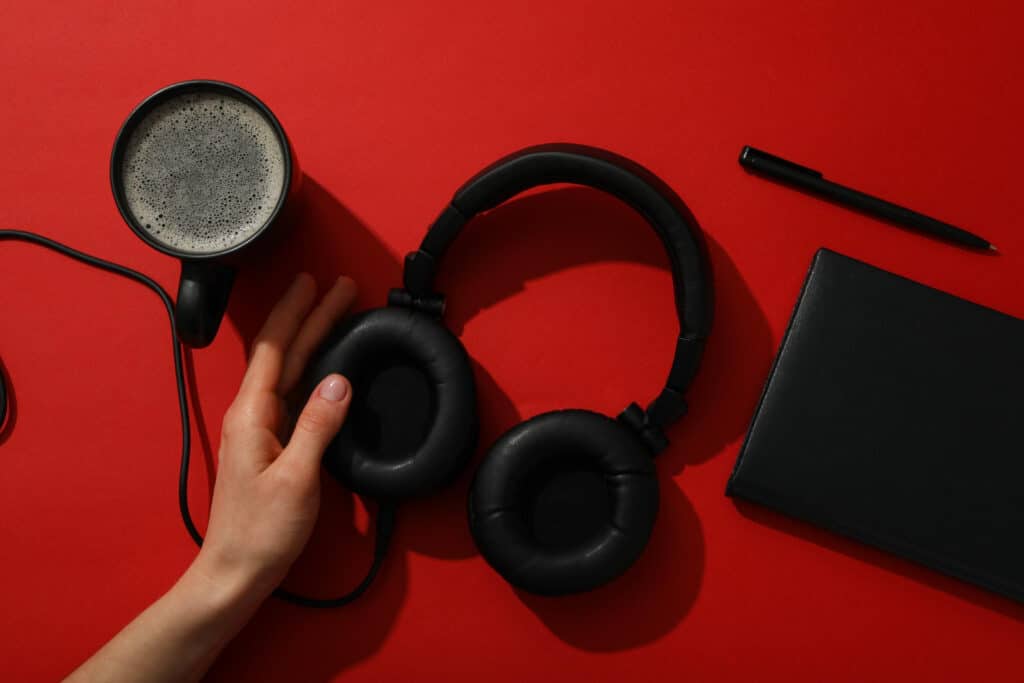 Imagem de uma xícara de café, um caderno, caneta e headset para trabalho híbrido sobre uma mesa vermelha.